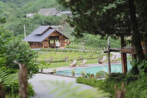 Un chalet en bois dotĂ© dâune piscine et de chaises longues, entourĂ© dâune vĂ©gĂ©tation luxuriante.