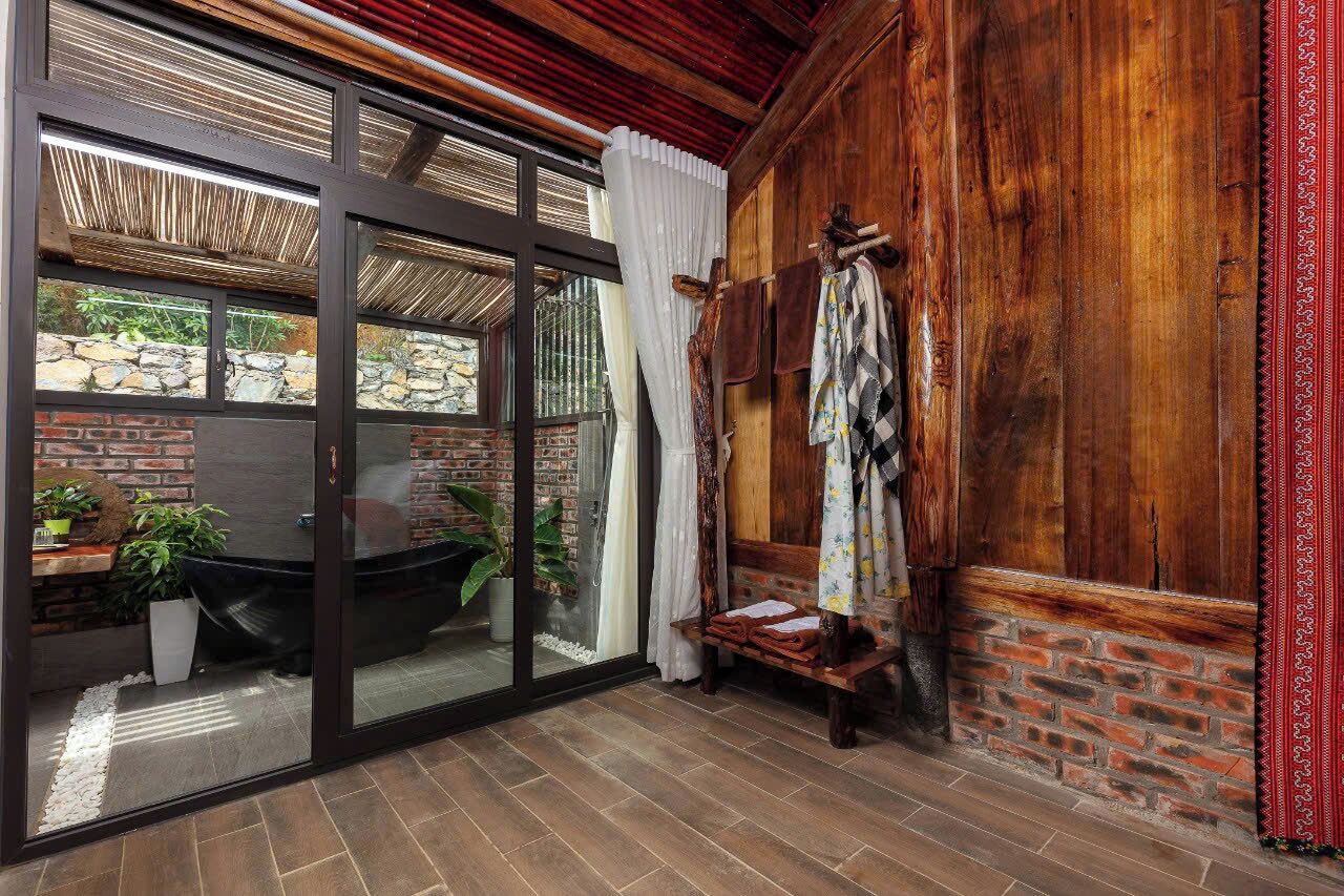 Een kamer met een glazen deur die uitkomt op een buitenruimte, een houten bank en een bakstenen muur.