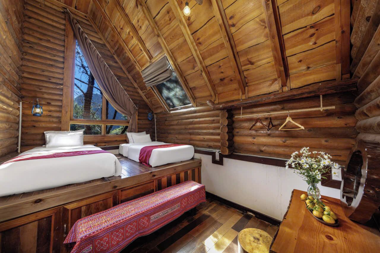 A log cabin room with two beds, a bench, a table with fruit, and a hanging light fixture.