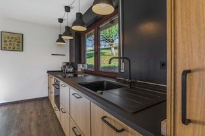 A modern kitchen with a black countertop, wooden cabinets, a black sink, and pendant lighting. - Holiday home in Grafenau with swimming pool (Grafenau)