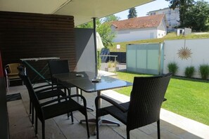 Eine Terrassengaststätte mit Tisch und Stühlen, einem überdachten Bereich und Blick auf eine Wohngegend mit Häusern und einem Garten.