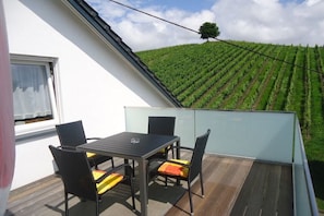Ein Balkon mit Tisch und Stühlen mit Blick auf ein Weinberg.