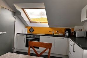 Eine kleine Küche mit Oberlicht, weißen Schränken und einem Holzbstuhl.