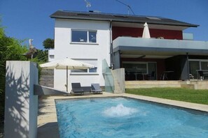 Ein modernes Haus mit Swimmingpool, zwei Liegestühlen und Sonnenschirm auf der Terrasse.
