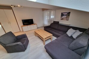 Ein stilvolles Wohnzimmer mit Sofa, Sessel, Fernseher und Couchtisch.