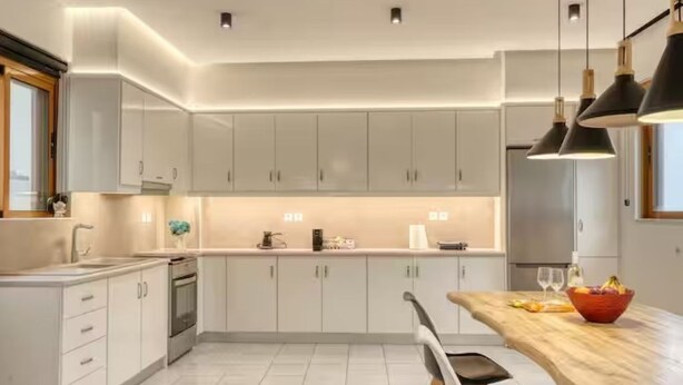 A modern kitchen with white cabinets, a wooden dining table, and pendant lighting. - Azure Seaside Living Kardamaina-10m from the sea (Kardamaina)
