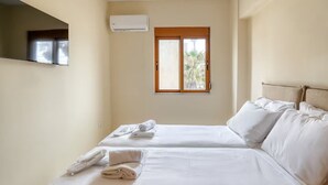 A hotel room with two beds, a window with a view, an air conditioning unit, and a flat-screen TV mounted on the wall. - Azure Seaside Living Kardamaina-10m from the sea (Kardamaina)