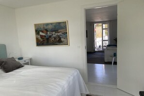 Ein Schlafzimmer mit Bett, Nachttisch, einem Gemälde und Blick in einen anderen Raum.