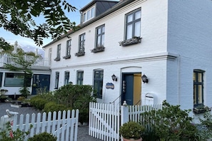 Ein weißes Gebäude mit blauer Tür, weißem Zaun und Kübelpflanzen.