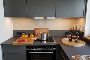 Eine moderne Küche mit Herd, Backofen und einem Holzer Schneidebrett mit Gemüse.
