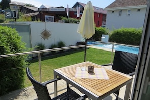 A balcony with a table, chairs, a yellow umbrella, and a view of a swimming pool. - A in the Sommertal guesthouse (Meersburg)
