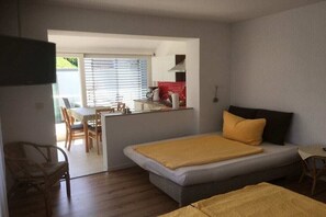 A bedroom with a bed, a small table, and a chair. There is a kitchenette in the background. - A in the Sommertal guesthouse (Meersburg)