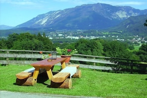 Ein Picknicktisch mit Bänken, ein Blumentopf und ein Laternen am Rasen, begrenzt durch einen Holzzaun.