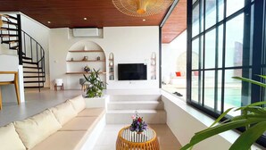 Uma sala de estar moderna com escada, televisão de tela plana e uma grande janela com vista para uma piscina.