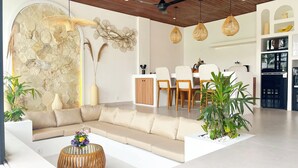Uma sala de estar moderna com um sofá seccional, uma área de jantar com mesa e cadeiras de madeira, e uma cozinha com eletrodomésticos.