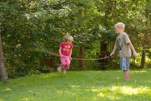 Two children playing with a rope swing in a grassy outdoor area surrounded by trees. - in the house on Hachelbach (Schliersee)