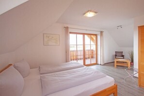 A bedroom with a bed, a chair, a small table, and a sliding glass door leading to an outdoor balcony. - Geiger - Säntisblick (Meersburg)