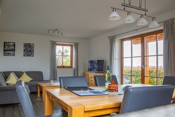 A modern living room with a sofa, dining table, chairs, a TV, and large windows with curtains. - Geiger - Säntisblick (Meersburg)
