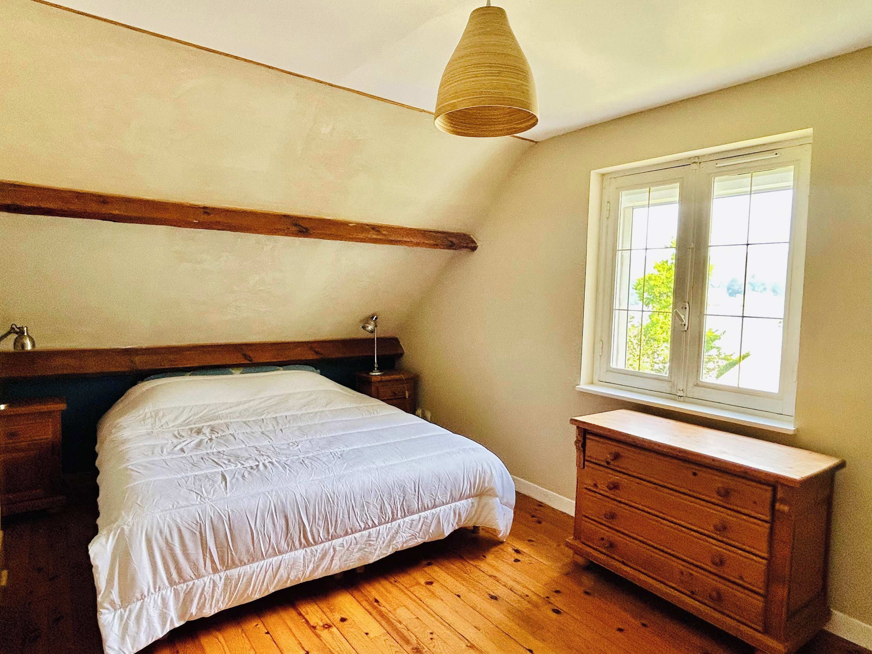 Ein Schlafzimmer mit einem hölzernen Bett, einem Schminktisch, einer Pendelleuchte und einem Fenster mit Blick.