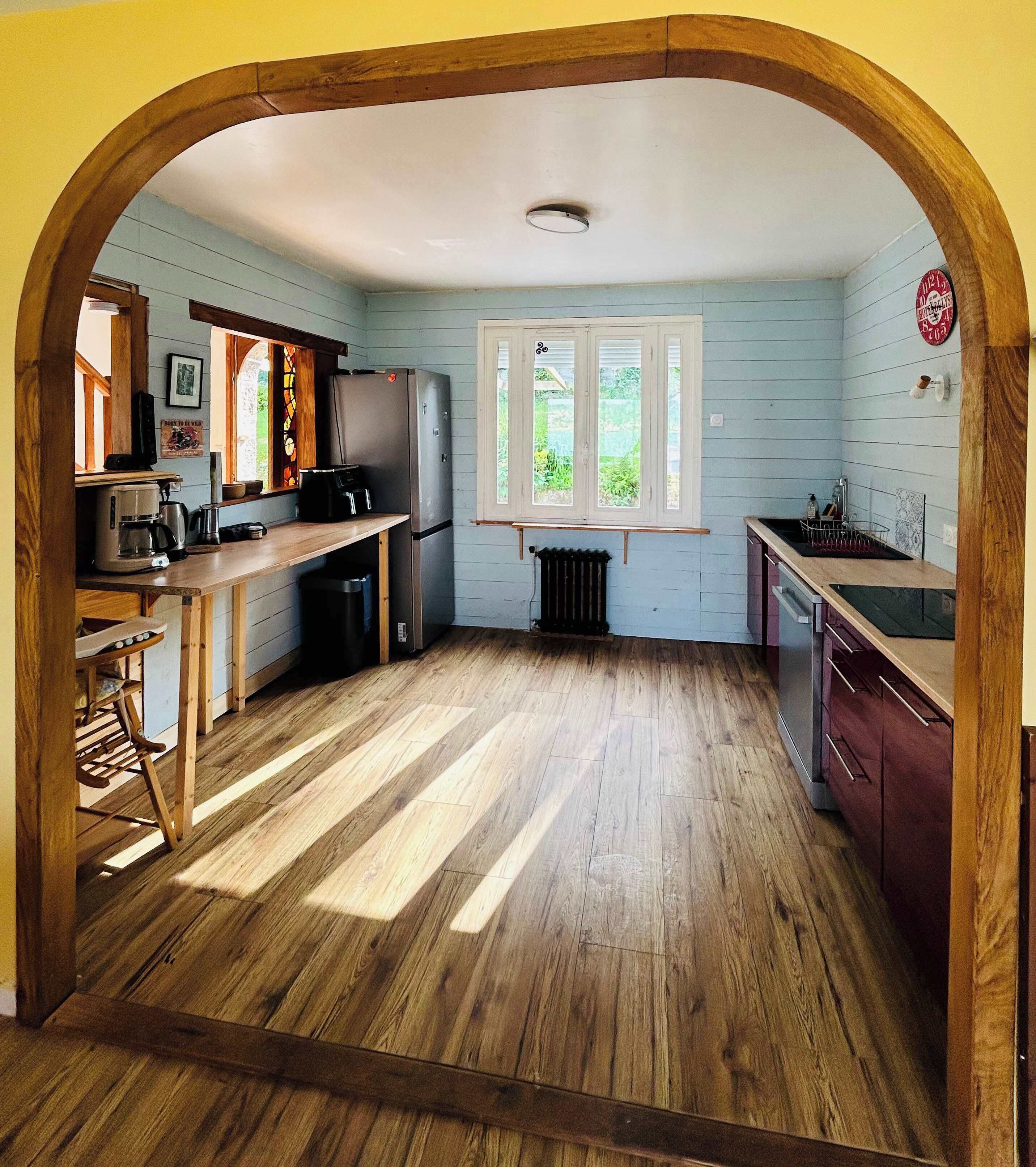 Une cuisine avec un plancher en bois, une fenêtre, un réfrigérateur et un évier.