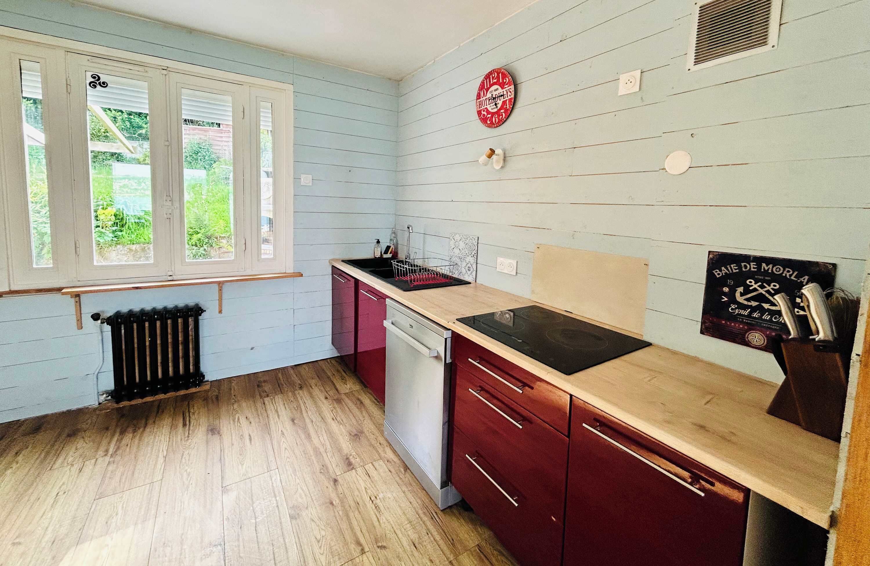 Una cocina con ventana, radiador, fregadero, lavavajillas y un reloj en la pared.