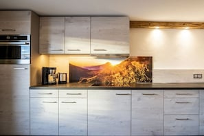 A modern kitchen with wooden cabinets, a built-in oven, and a large painting of a sunset. - Holiday apartment with 3 bedrooms (Oberstdorf-Schöllang)