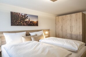 A hotel room with two beds, a wooden wardrobe, and a cityscape painting on the wall. - Holiday apartment with 3 bedrooms (Oberstdorf-Schöllang)