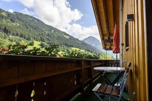 Un balcon en bois, agrémenté d’une table et de chaises, qui offre une vue sur un paysage montagneux.