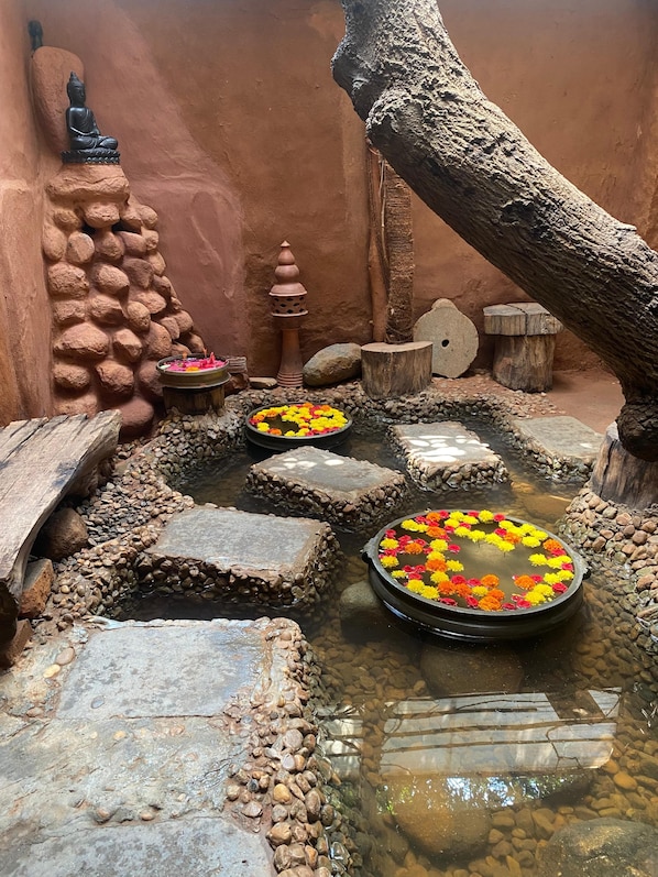 A serene indoor garden with a Buddha statue, a small water feature, and a rustic stone wall.