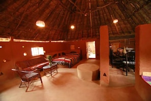 A thatched-roof room with a sofa, a small table, and a chair.