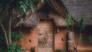 Una casetta rustica con tetto di paglia, una porta in legno con decorazioni geometriche e un rilievo a forma di volto sulla parete.