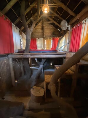 Un interior rústico con techo de madera, cama con cortinas rojas y una lámpara colgante.