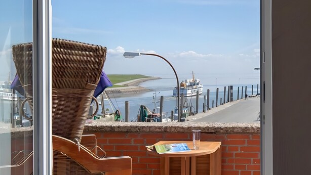 Un balcon agrémenté de meubles en osier, d’une table et offrant une vue sur le bord de l’eau, o ù l’on aperçoit un bateau.