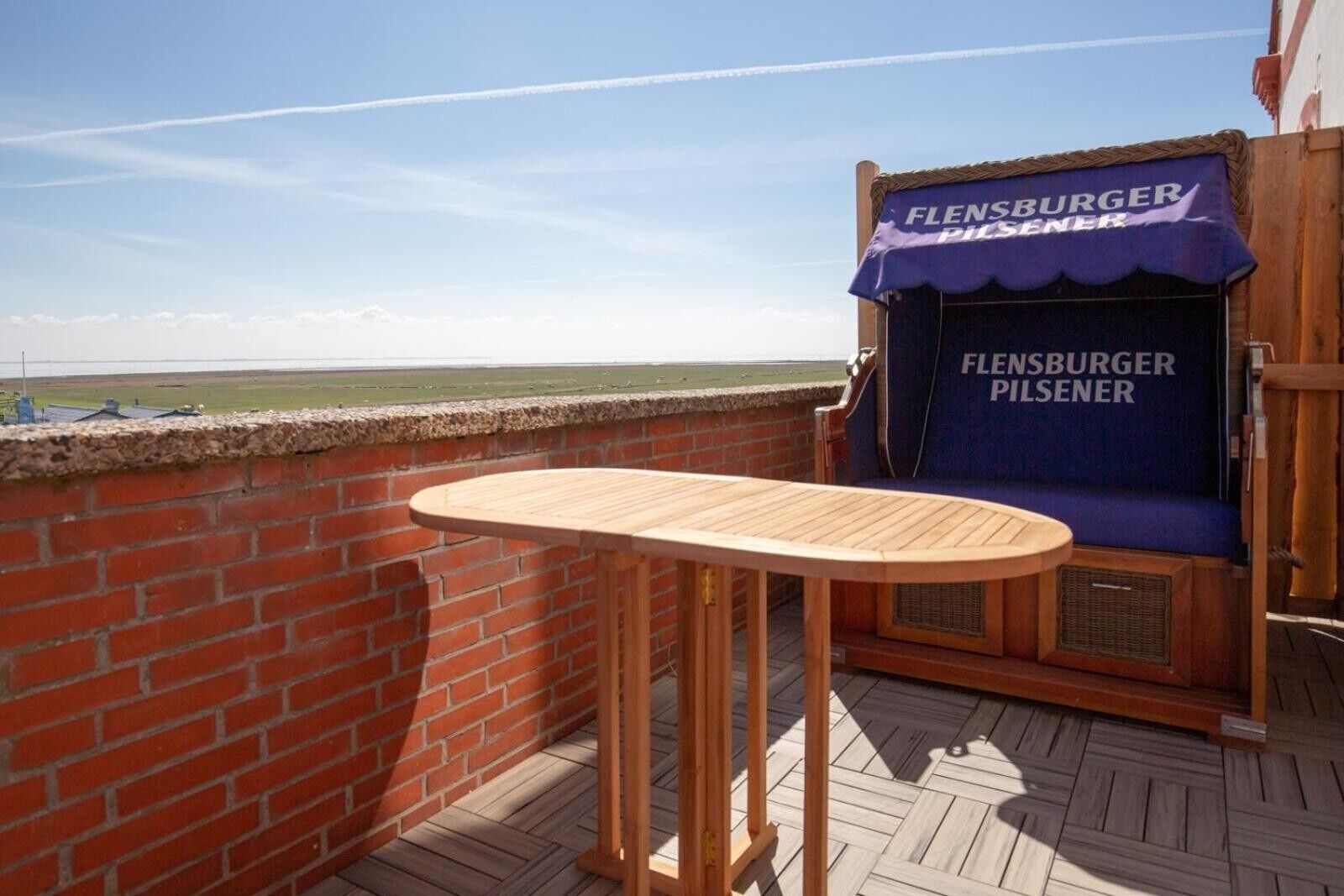 Ein Balkon mit einem Holztisch und einer Sitzecke, mit einem Schild für 'Fleinsburger Pilsener'.