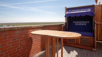 Ein Balkon mit einem Holztisch und einer Sitzecke, mit einem Schild für 'Fleinsburger Pilsener'.