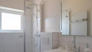 Ein modernes Badezimmer mit Duschkabine aus Glas, einer weißen Toilette, einem hölzernen Waschtisch mit Spiegel und einem Fenster für Tageslicht.