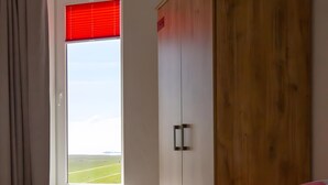 Ein Schlafzimmer mit großem Fenster, einem Holzschrank und einem Bett mit Kissen.