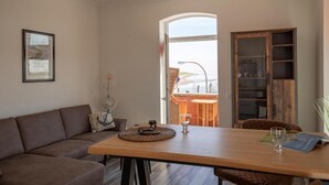 Ein Wohnzimmer mit Holztisch, braunem Sofa, Bücherregal und Blick ins Freie.