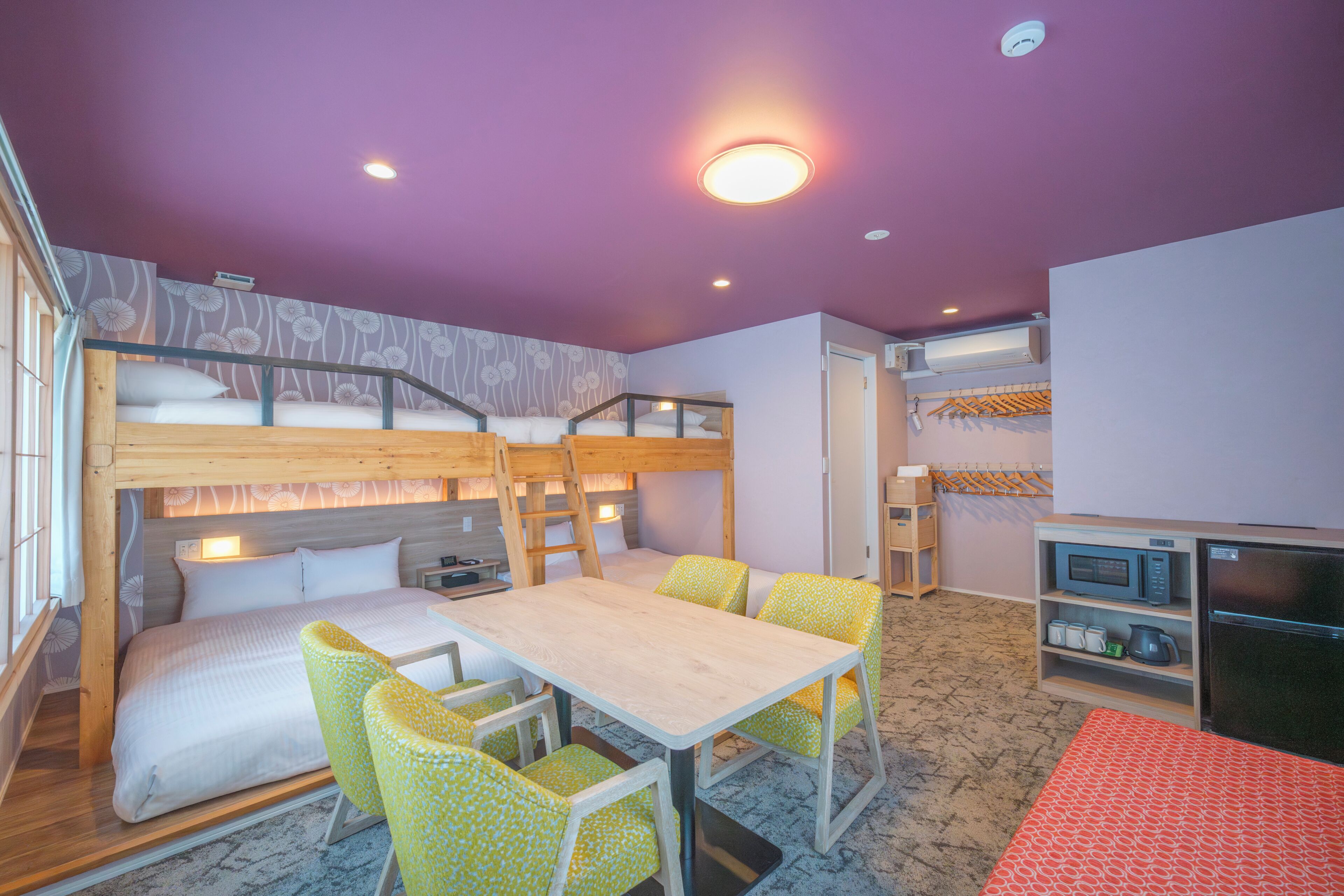 Habitación con literas, una mesa, sillas, un microondas y un refrigerador.