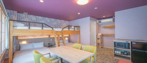 Habitación con literas, una mesa, sillas, un microondas y un refrigerador.