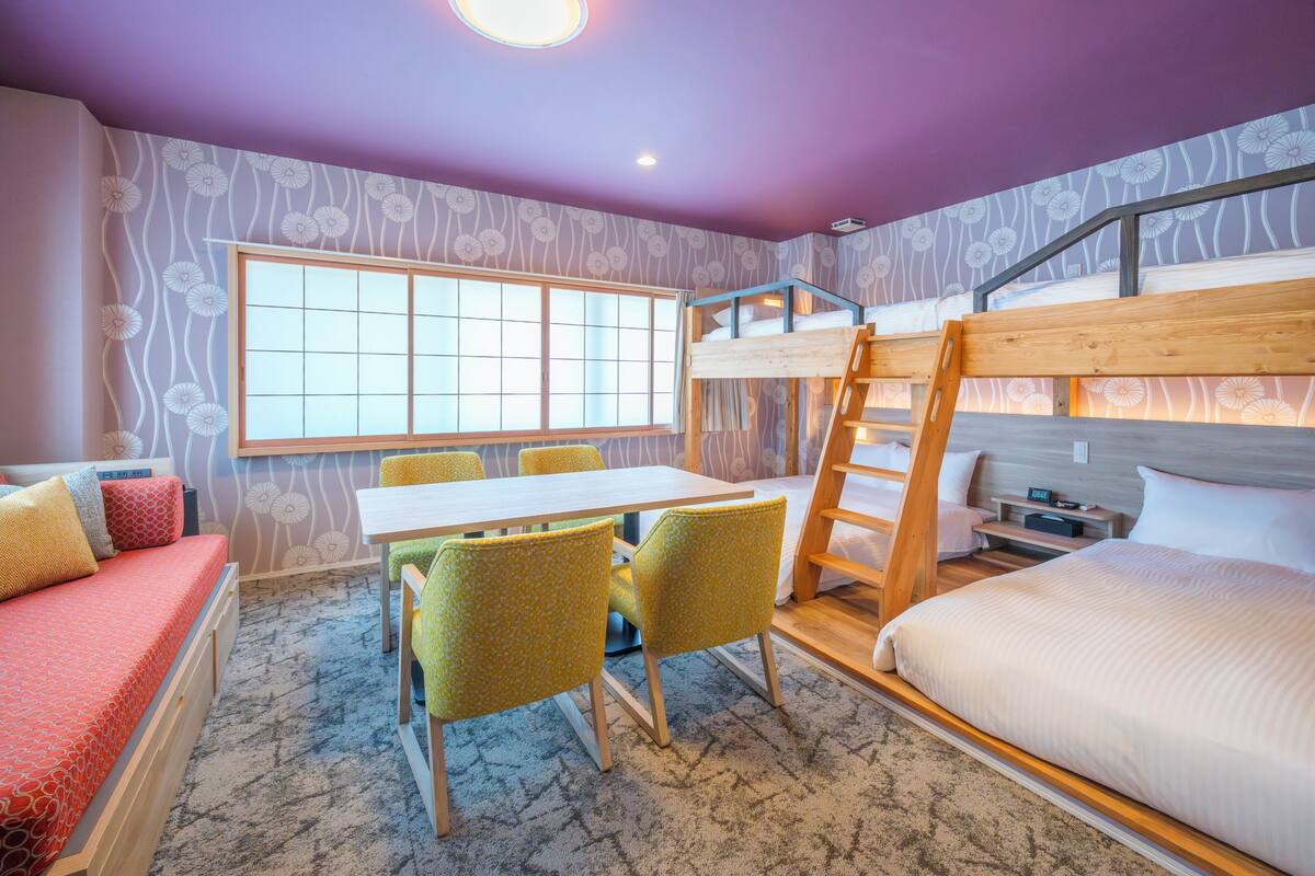 A room with a bunk bed, a desk with chairs, a window, and a carpeted floor.