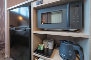 Een kleine keuken met een koelkast, magnetron, waterkoker en een dienblad met theezakjes en mokken.