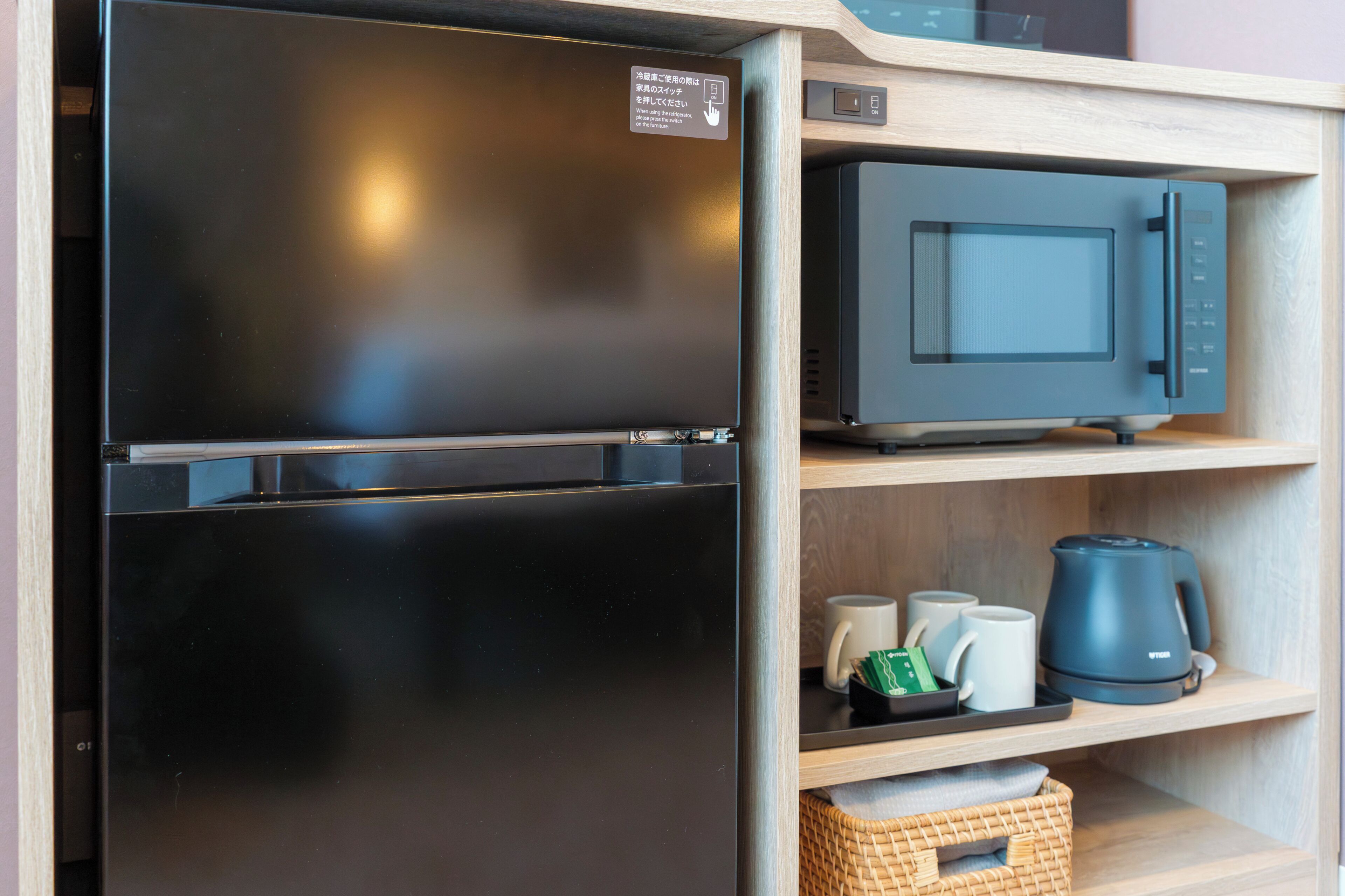 A compact kitchen with a black refrigerator, a microwave, and a coffee maker on a wooden shelf.