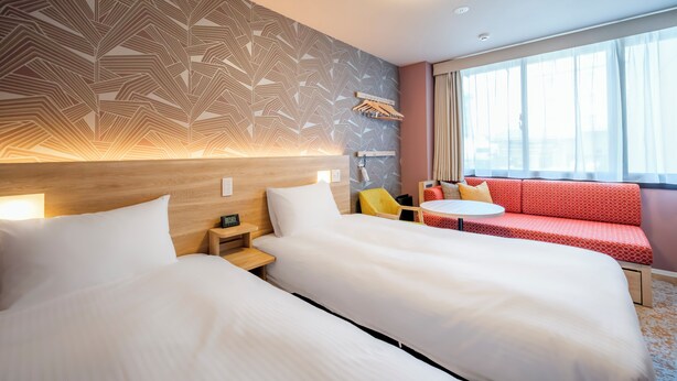 Habitación de hotel con dos camas, un sofá, una mesita y una ventana con cortinas.