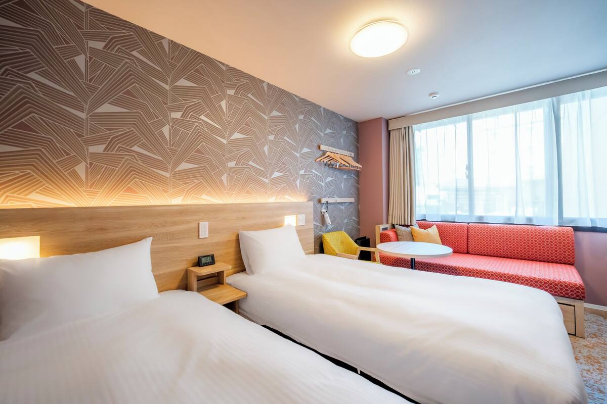 A hotel room with two beds, a sofa, a small table, and a window with curtains.