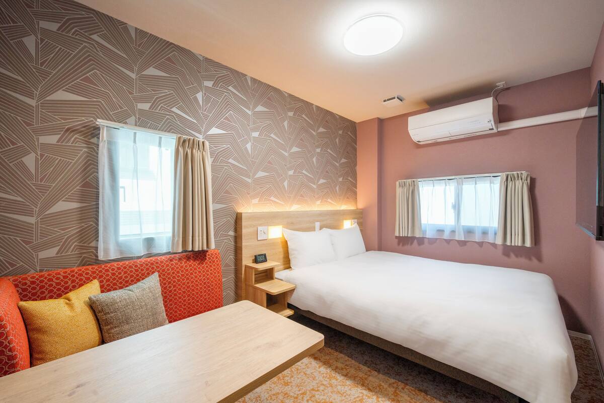 A hotel room with a bed, a sofa, a nightstand, and a table.