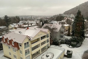 Ein mehrstöckiges Hotel mit einem Balkon im zweiten Stock, eine verschneite Landschaft und Blick auf die umliegende Stadt.