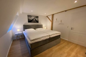 Ein Schlafzimmer mit Bett, Nachttisch, Wandkunst, Holztür und einer Lampe.