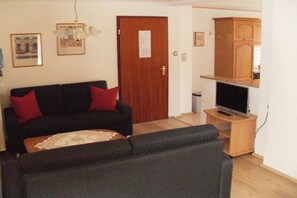 Ein Wohnzimmer mit einer Couch, einem Couchtisch, einem Fernseher auf einem Schrank und einer Tür mit einem Schild.