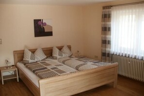 Une chambre à coucher avec un lit en bois, une table de chevet, une œuvre d’art accrochée au mur et une fenêtre avec des rideaux.